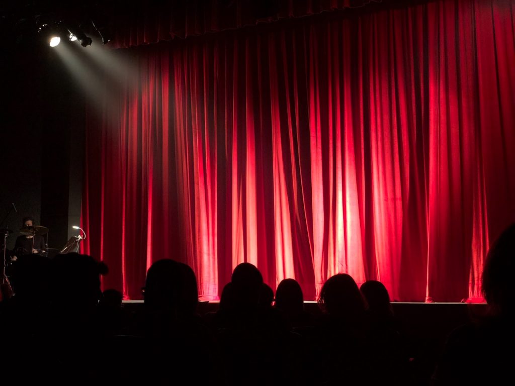 a group of people sitting on a stage with red curtains