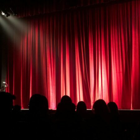 a group of people sitting on a stage with red curtains
