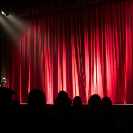 a group of people sitting on a stage with red curtains