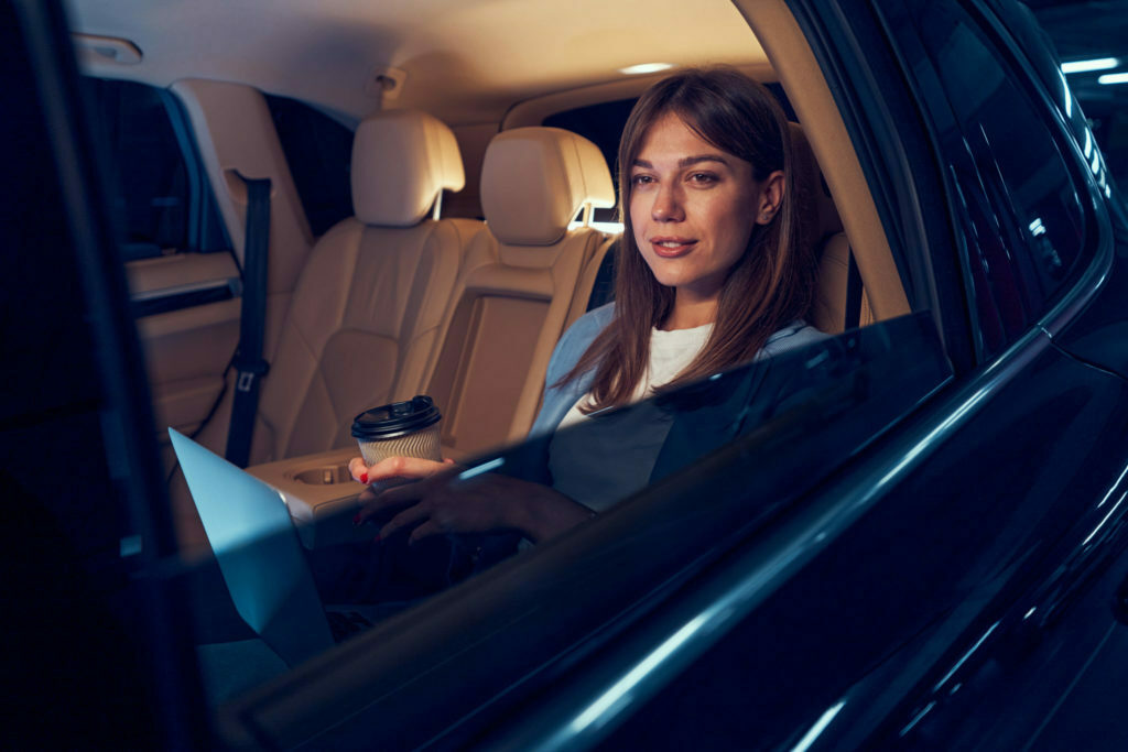 Smiling woman with coffee cup sitting in car